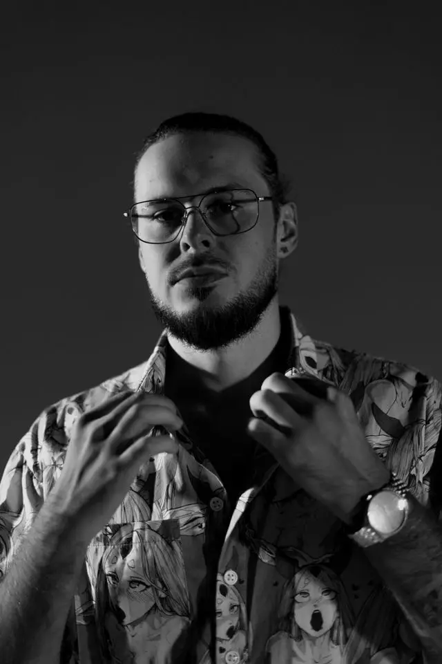 Studio portrait of OPPAACHA in glasses and a patterned blue shirt