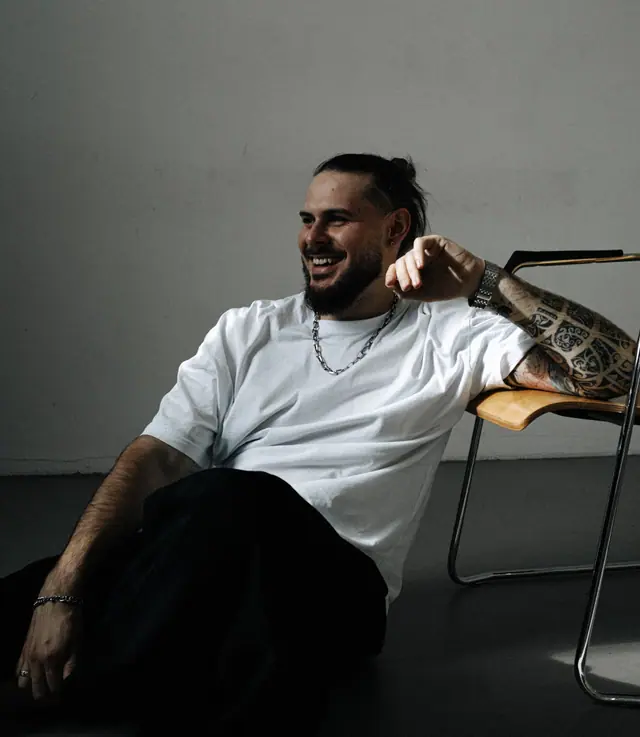 OPPAACHA leaning back in a chair, smiling, white t-shirt