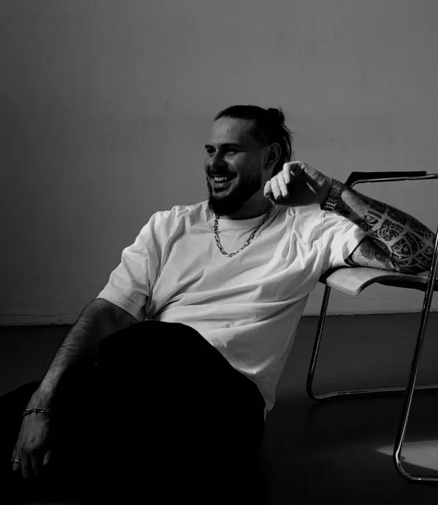 OPPAACHA leaning back in a chair, smiling, white t-shirt